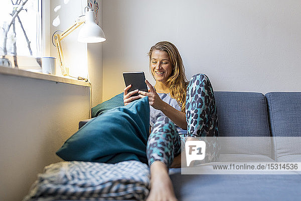 Happy young woman sitting on couch at home using tablet