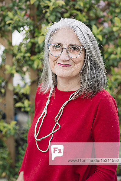 Porträt einer lächelnden älteren Frau mit grauen Haaren  die einen roten Pullover und eine Brille trägt