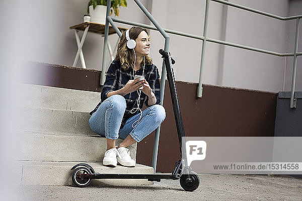 Young womanwith electric scooter  sitting on stairs  listening music