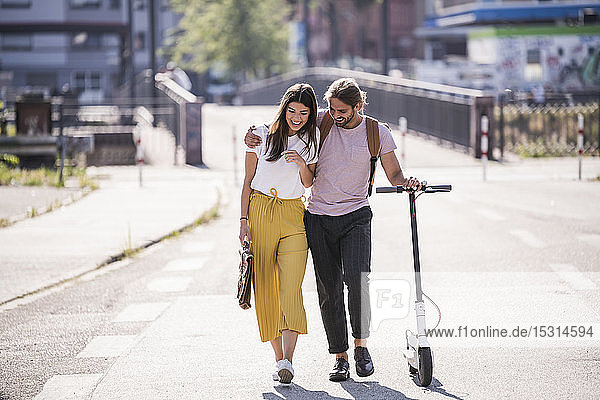 Glückliches junges Paar mit Elektroroller auf der Straße