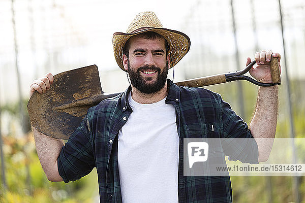 Portrait of smiling young man holding a shovel in a greenhouse