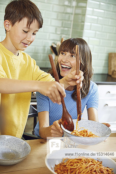 Mother eating spaghetti with her son in the kitchen