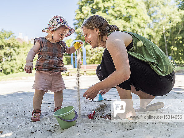 Kleines Mädchen mit seiner Mutter im Sandkasten auf dem Spielplatz