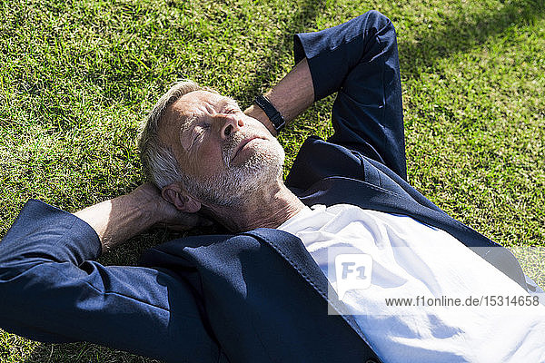 Senior businessman lying in grass with closed eyes
