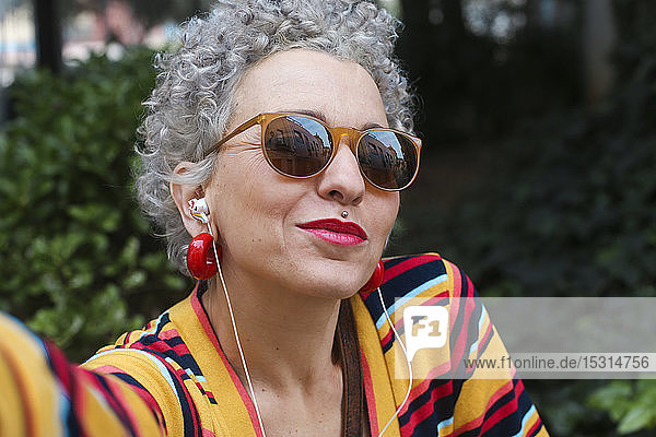 Porträt einer durchbohrten reifen Frau mit Sonnenbrille und Kopfhörern