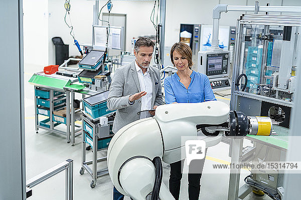 Geschäftsmann mit Tablette und Frau im Gespräch am Montageroboter in einer Fabrik
