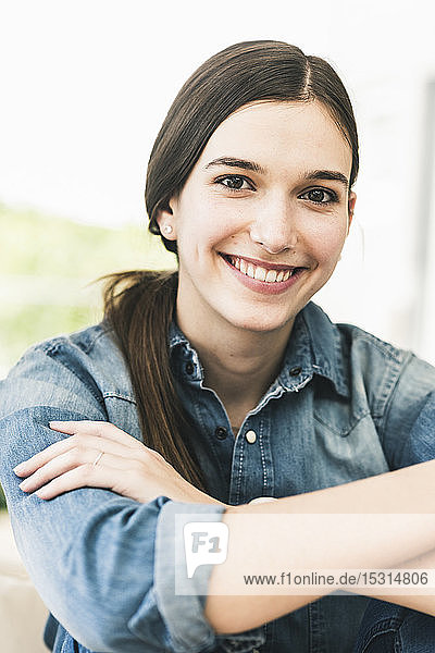 Porträt einer lächelnden jungen Frau  die zu Hause ein Jeanshemd trägt