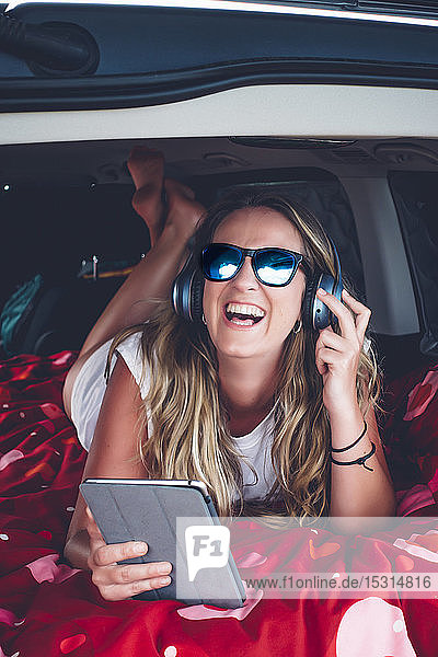 Hübsche blonde Frau mit Sonnenbrille und Kopfhörer beim Zelten in einem Lieferwagen mit Tablette