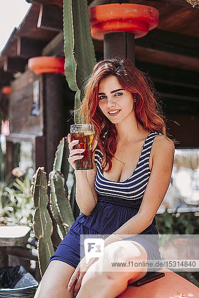 Junge Frau mit einem Getränk auf einer Bank im Freien sitzend