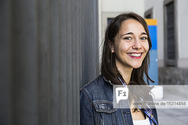 Young smiling woman looking at camera  standing at wall
