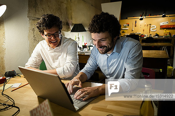 Two happy colleagues using laptop in the dark together