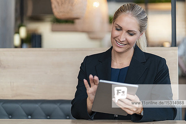 Portrait of smiling blond businesswoman using digital tablet in a coffee shop