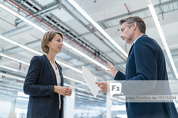 Geschäftsmann und Geschäftsfrau besprechen Plan in einer Fabrikhalle