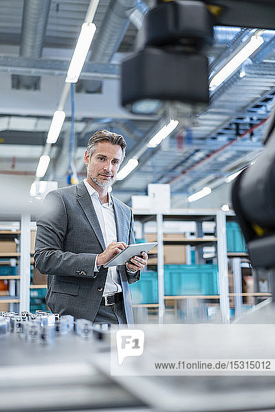 Geschäftsmann mit Tablette in einer modernen Fabrikhalle mit Blick auf Roboter