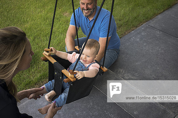 Happy family with baby girl in a swing