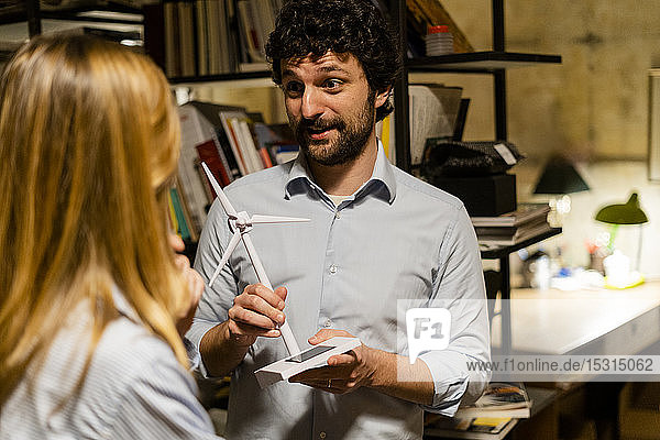 Businessman with wind turbine model talking to colleague in office