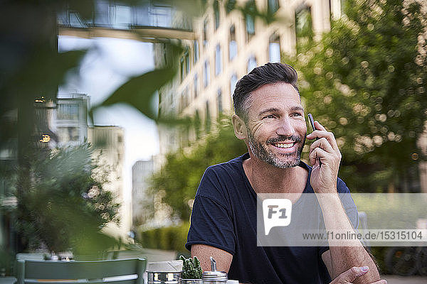 Smiling mature man using smartphone  sitting at street cafe
