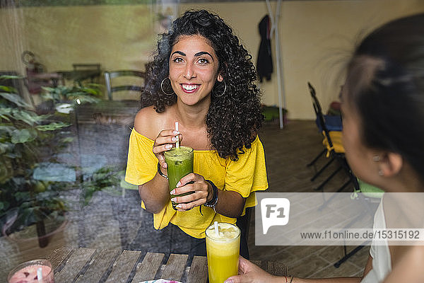 Porträt einer lächelnden jungen Frau mit einem gesunden Getränk in einem Bistro
