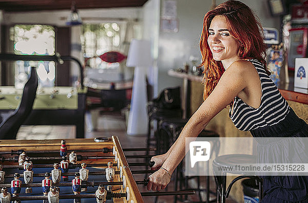 Portrait of happy young woman playing foosball in a sports bar