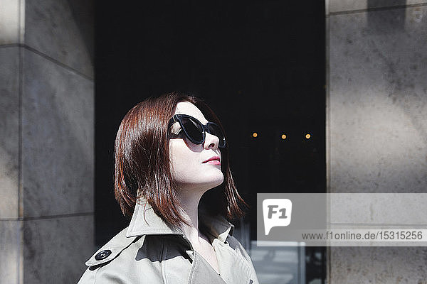 Porträt einer stilvollen Frau mit Sonnenbrille und Trenchcoat