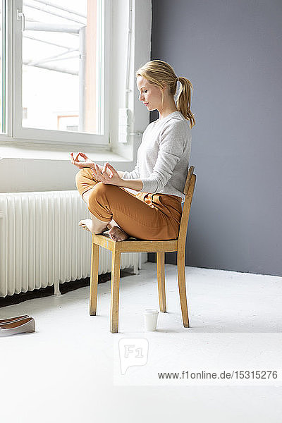 Junge Frau  die im Büro auf einem Stuhl sitzt und Yoga praktiziert