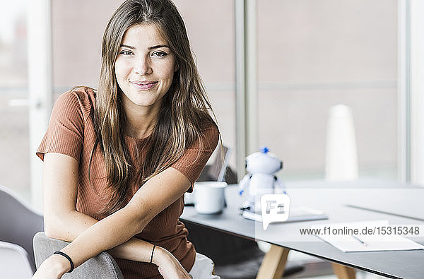 Porträt einer lächelnden jungen Geschäftsfrau  die im Büro am Schreibtisch sitzt