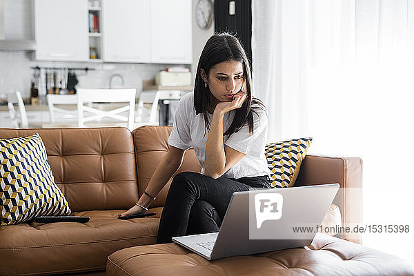 Junge Frau sitzt zu Hause auf einer Couch und benutzt einen Laptop