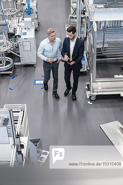 Two businessmen with clipboard talking in a factory