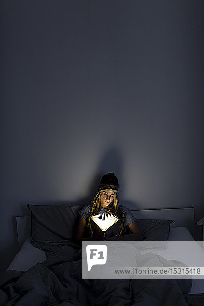 Young woman reading illuminated book in bed at home
