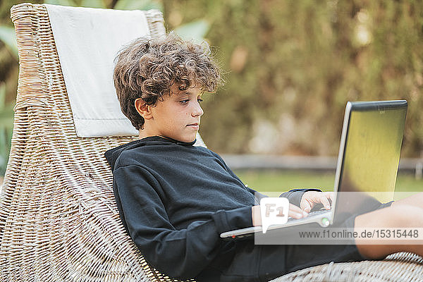 Entspannter Junge mit Laptop im Aufenthaltsraum im Garten