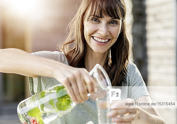 Porträt einer glücklichen Frau  die aufgegossenes Wasser in ein Glas gießt