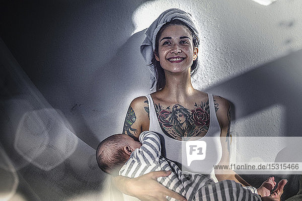 Lächelnde tätowierte junge Frau  die ihr Baby zu Hause hält
