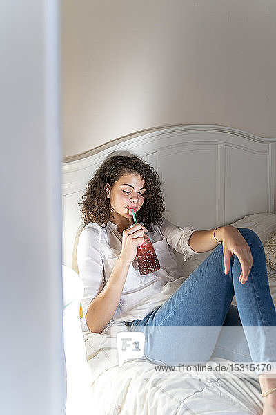Entspannte junge Frau liegt mit gesundem Getränk im Bett