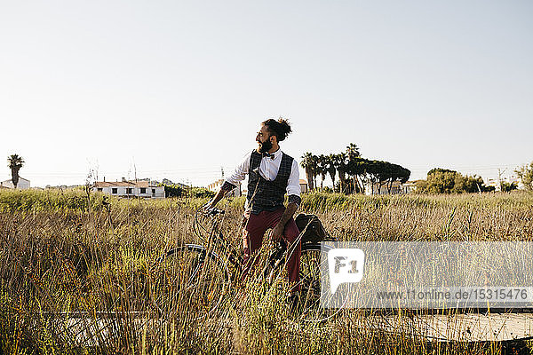 Well dressed man with his bike on a wooden walkway in the countryside having a break