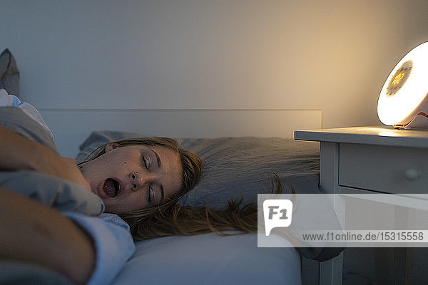 Young woman lying in bed at home at night yawning