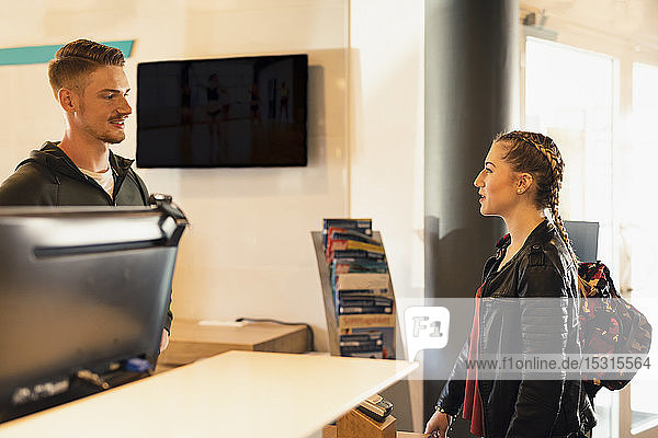 Young woman talking to coach at front desk of a gym