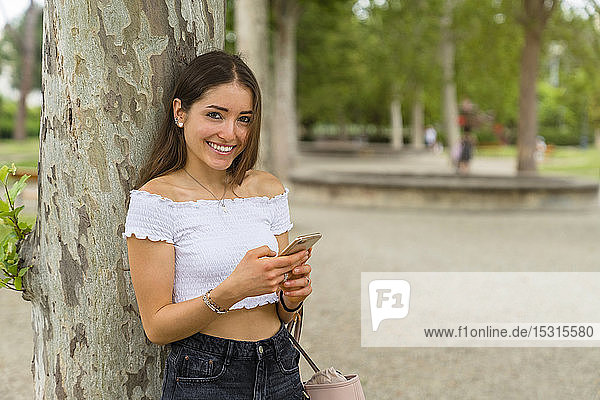 Porträt einer jungen Frau mit Smartphone im Park