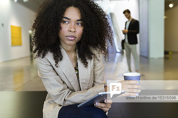 Junge Geschäftsfrau mit Kaffee und Tablette zum Mitnehmen in einem Foyer