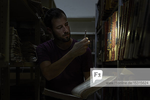 Man among bookshelves lighting books with his smartphone  National library  Maputo  Mocambique