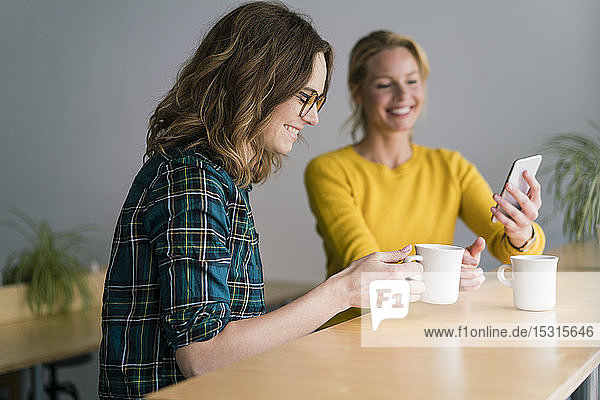 Two girlfriends sitting in coffee shop  drinking coffee  using smartphone