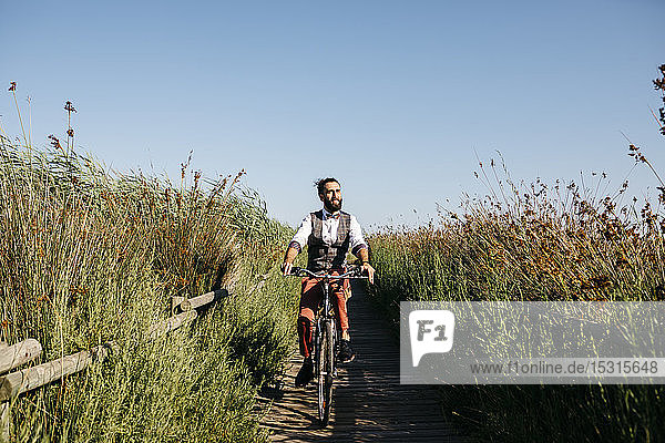 Gut gekleideter Mann mit seinem Fahrrad auf einem Holzsteg auf dem Land nach der Arbeit