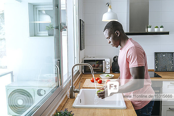 Junger Mann wäscht Kopfsalat in der Küche