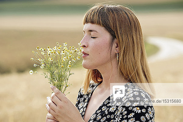 Young woman with eyes closed smelling bunch of chamomile flower