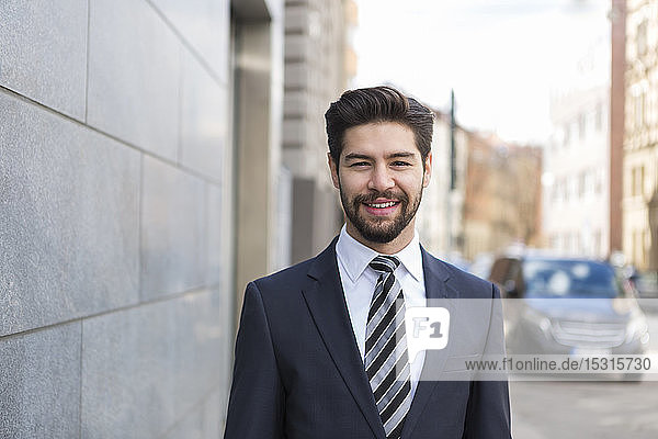 Portrait of bearded young businessman wearing blue suit jacket and tie in the city