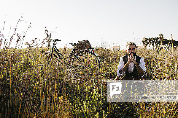 Gut gekleideter Mann  der auf einem Holzsteg auf dem Land neben einem Fahrrad sitzt