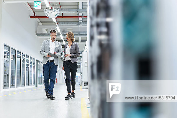 Businesswoman and businessman with tablet walking and talking in a modern factory
