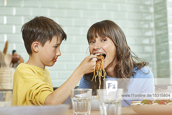 Son feeding mother with spaghetti in the kitchen