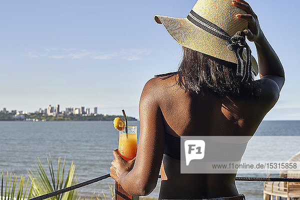 Junge Frau mit einem Drink an der Uferpromenade mit Blick auf die Skyline von Maputo  Mosambik