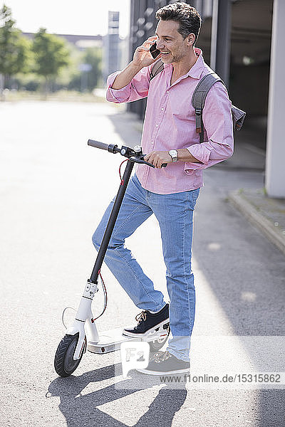 Businessman using smartphone  standing on E-Scooter