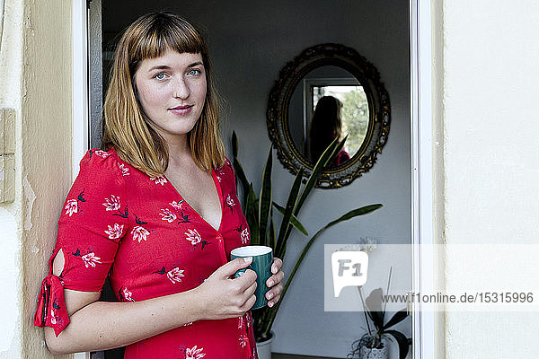 Porträt einer jungen Frau mit Tasse Kaffee auf dem Balkon stehend